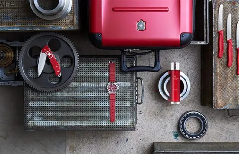 מגוון מוצרי המותג ויקטורינוקס בגווני אדום: בושם, מזוודה, סכינים, שעון ואולר- להצגת המותג