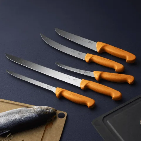 סכיני SWIBO על משטח עבודה לצד דג וקרשי חיתוך