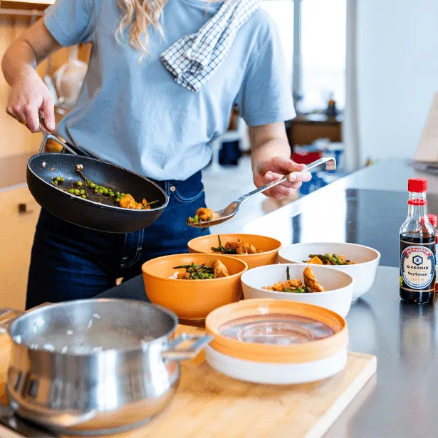 קטגוריית קופסאות אחסון למטבח אישה מעבירה אוכל לקופסאות בגווני כתום ולבן